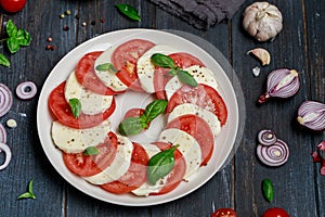 Delicious italian caprese salad with ripe tomatoes, fresh basil and mozzarella cheese on wooden rustic background. Italian caprese