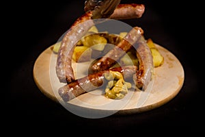 Delicious Italian sausage cooked on the grill with browned diced potatoes placed on a wooden cutting board with drops of mustard w