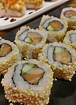 Delicious Japanese food Sushi Roll Maki of Red Salmon and Green avocado with sesame on the black plate