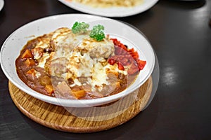 Delicious Japanese hamburg curry Serve with and mozzarella cheese on top with Rice, curry Rice in white plate on a black table