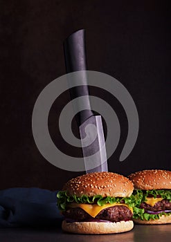 Delicious juicy burger with knife on dark background