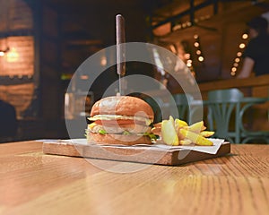 Delicious juicy chef cheeseburger served with fries on a rustic wooden board on a table in bar or restaurant