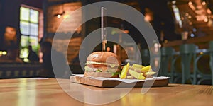 Delicious juicy chef cheeseburger served with fries on a rustic wooden board on a table in bar or restaurant