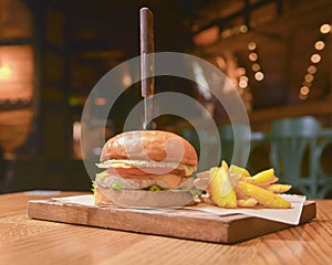 Delicious juicy chef cheeseburger served with fries on a rustic wooden board on a table in bar or restaurant.