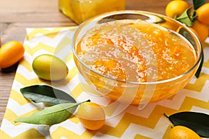 Delicious kumquat jam in bowl and fresh fruits on table, space for text