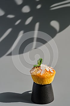 Delicious lemon muffin or cupcake with frosting and almond flakes. Homemade magdalena on gray neutral background, dish serving