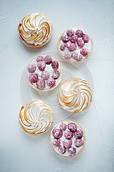 Delicious lemon and raspberry tartlets with meringue on a white vintage plate. Sweet treat on a light blue background. Flat lay an