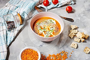 Delicious lentils soup with heavy cream on concrete table with red pepper, bread toasts.