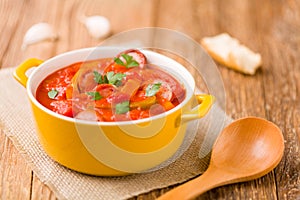 Delicious letcho with fresh vegetables, served in a yellow pot with the fresh bun