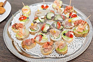 Delicious little sandwiches bites with bacon, cherry tomato, olives, cucumber, lettuce and corn on a tray