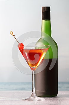 Delicious looking homemade cocktail with cherries in a martini glass in front of a wine bottle