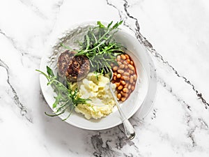 Delicious lunch - chicken cutlets, mashed potatoes, beans tomato sauce and arugula salad on a light background, top view