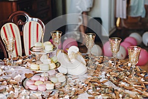 Delicious macarons on beautiful vintage stand and champagne glasses on table with gold and silver confetti and duck. Luxury