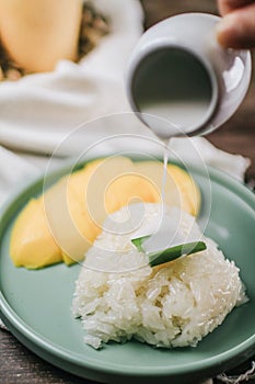 Delicious mango sticky rice serve with coconut milk on wooden table.