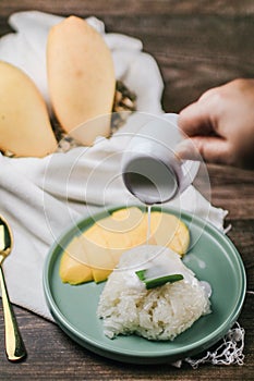 Delicious mango sticky rice serve with coconut milk on wooden table.