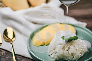 Delicious mango sticky rice serve with coconut milk on wooden table.