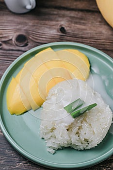 Delicious mango sticky rice serve with coconut milk on wooden table.