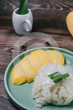 Delicious mango sticky rice serve with coconut milk on wooden table.