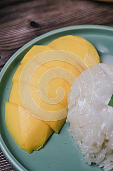 Delicious mango sticky rice serve with coconut milk on wooden table.