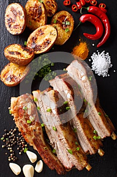 Delicious meal: fried ribs with baked potatoes and spices close-up on the table. vertical view from above