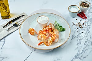 Delicious Mediterranean appetizer - grilled tiger prawns with garlic sauce, served in a plate on a marble background. Seafood