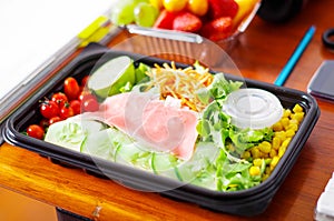 Delicious mediterranean-Style fresh salad with ham in a plastic box on wooden table