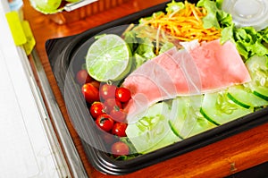 Delicious mediterranean-Style fresh salad with ham in a plastic box on wooden table