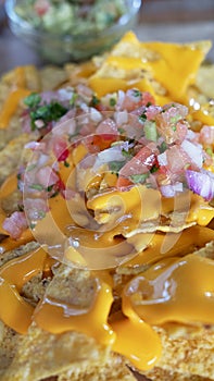 Delicious Mexican cuisine dish, nachos with melted cheddar cheese, roughly chopped tomatoes, onions, peppers and coriander leaves
