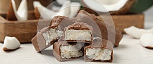 Delicious milk chocolate candy bars with coconut filling on white wooden table, closeup. Banner design