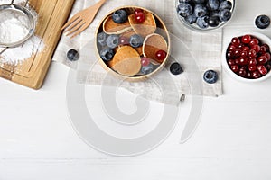 Delicious mini pancakes cereal with berries served on white table, flat lay. Space for text