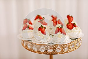 Delicious mini Pavlova meringue cakes with fresh strawberry on gold festive tray