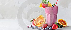 A delicious mixed berry smoothie decorated with a strawberry, orange wedge, and blueberries on a white background.