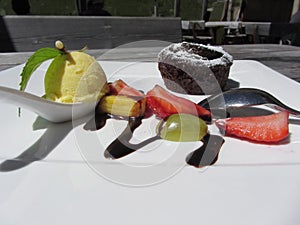 Delicious molten chocolate cake with fresh fruit and vanilla ice cream on rustic outdoor wooden table at summer
