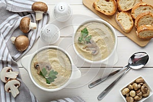 Delicious mushroom cream soup with parsley served on white wooden table, flat lay