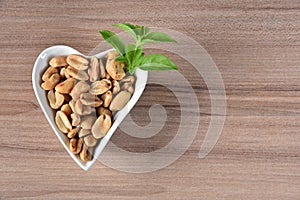 Delicious and nutritious peanuts, peeled in a heart-shaped bowl with overhead view isolated on wooden table