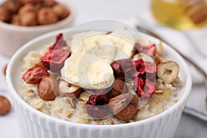 Delicious oatmeal with freeze dried berries, banana and hazelnuts on table, closeup