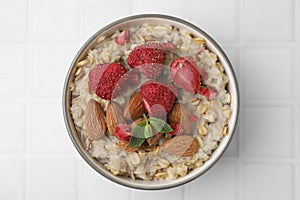 Delicious oatmeal with freeze dried strawberries, almonds and mint on white tiled table, top view