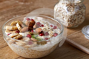 Delicious oatmeal porrige with fruits in glass bowl over rustic wooden background, shallow depth of field, close-up.