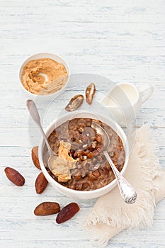 Delicious oatmeal in a white bowl, dates fruits, cocoa and vegan milk