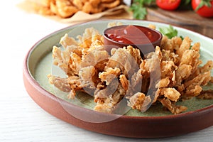 Delicious onion blossom with ketchup served on white wooden table, closeup