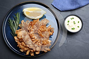 Delicious onion blossom served with lemon and sauce on black table, flat lay