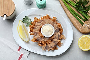 Delicious onion blossom served with lemon and sauce on white table, flat lay