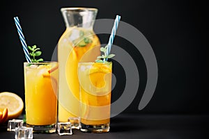 Delicious orange juice with ice, mint and fresh fruits on black table background with copy space