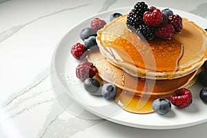 Delicious pancakes with berries, honey or maple syrup. Homemade pancakes and sweet syrup on white plate isolated.