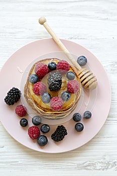 Delicious pancakes with berries and honey on a pink plate, top view.