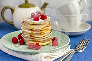 Delicious pancakes with raspberries and tea cups on the table.