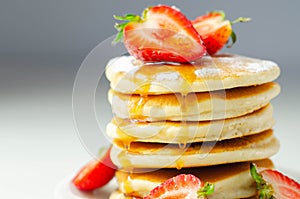 Delicious pancakes stacked with fresh sweet strawberries, topped with maple syrup