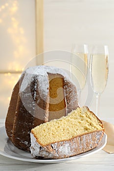 Delicious Pandoro cake decorated with powdered sugar and glasses of sparkling wine on white wooden table. Traditional Italian