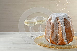 Delicious Pandoro cake decorated with powdered sugar and sparkling wine on white wooden table, space for text. Traditional Italian