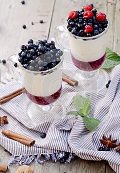 Delicious parfait dessert with bilberry, milk souffle and jello layers. Frozen treat in a glass on rustic wooden